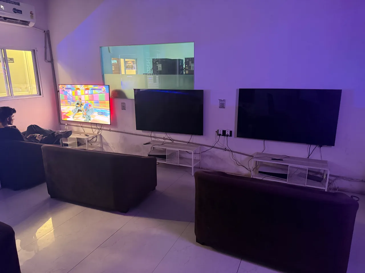 Console room at Intencity Undri: sofas facing wall-mounted TVs, with a player mid-game