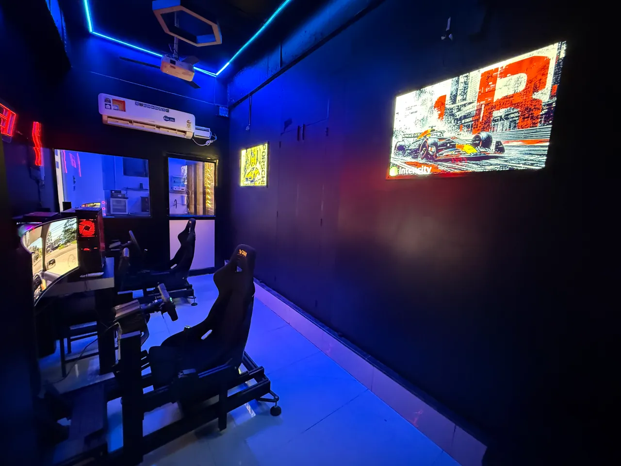 The two racing seats seen from behind, with lit racing artwork on the wall of the Sim Racing room at Intencity Undri