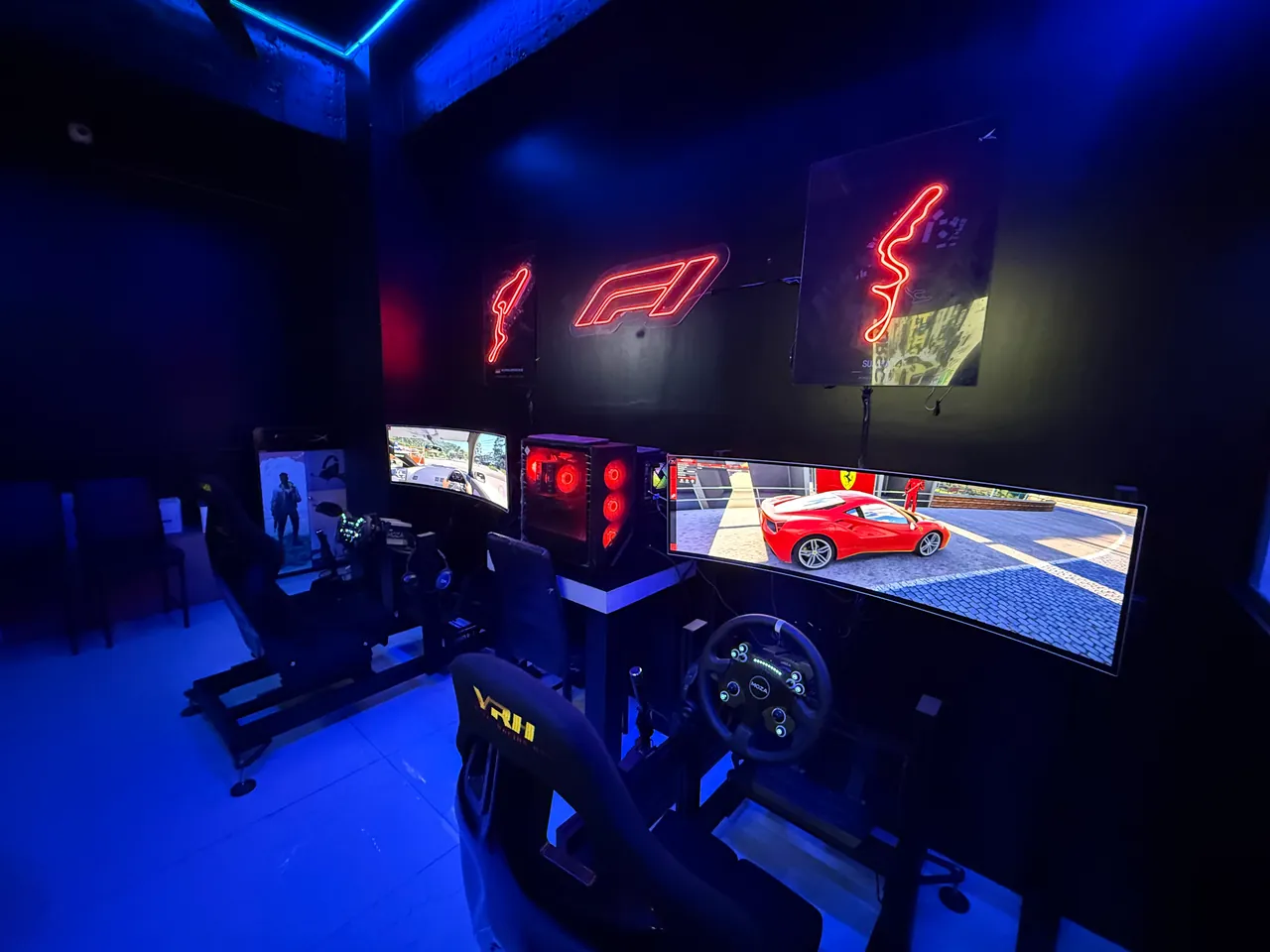 Sim racing wheel and seat in front of a curved ultrawide screen, under red neon track signs at Intencity Undri